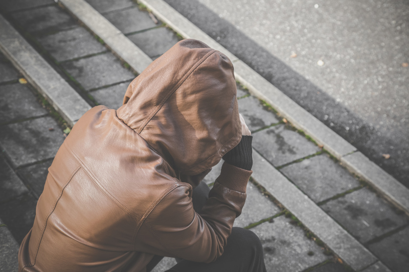 Young person in brown leather jacket with hood sitting on stairs and suffering from life difficulties, broken heart or psychological problems. Dark, gloomy thoughts. Social isolation. Test Therapist