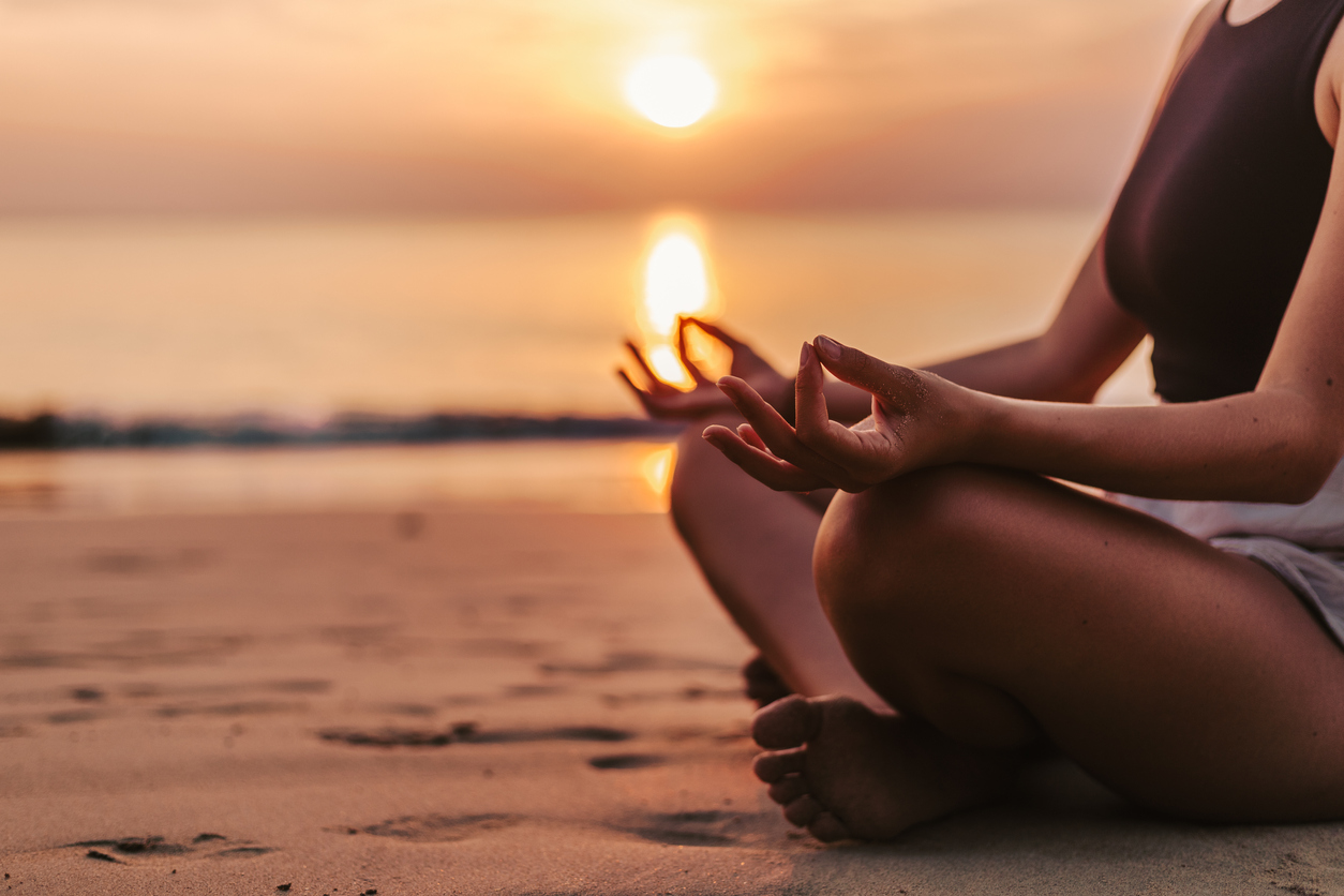 Woman meditating on the beach at sunset