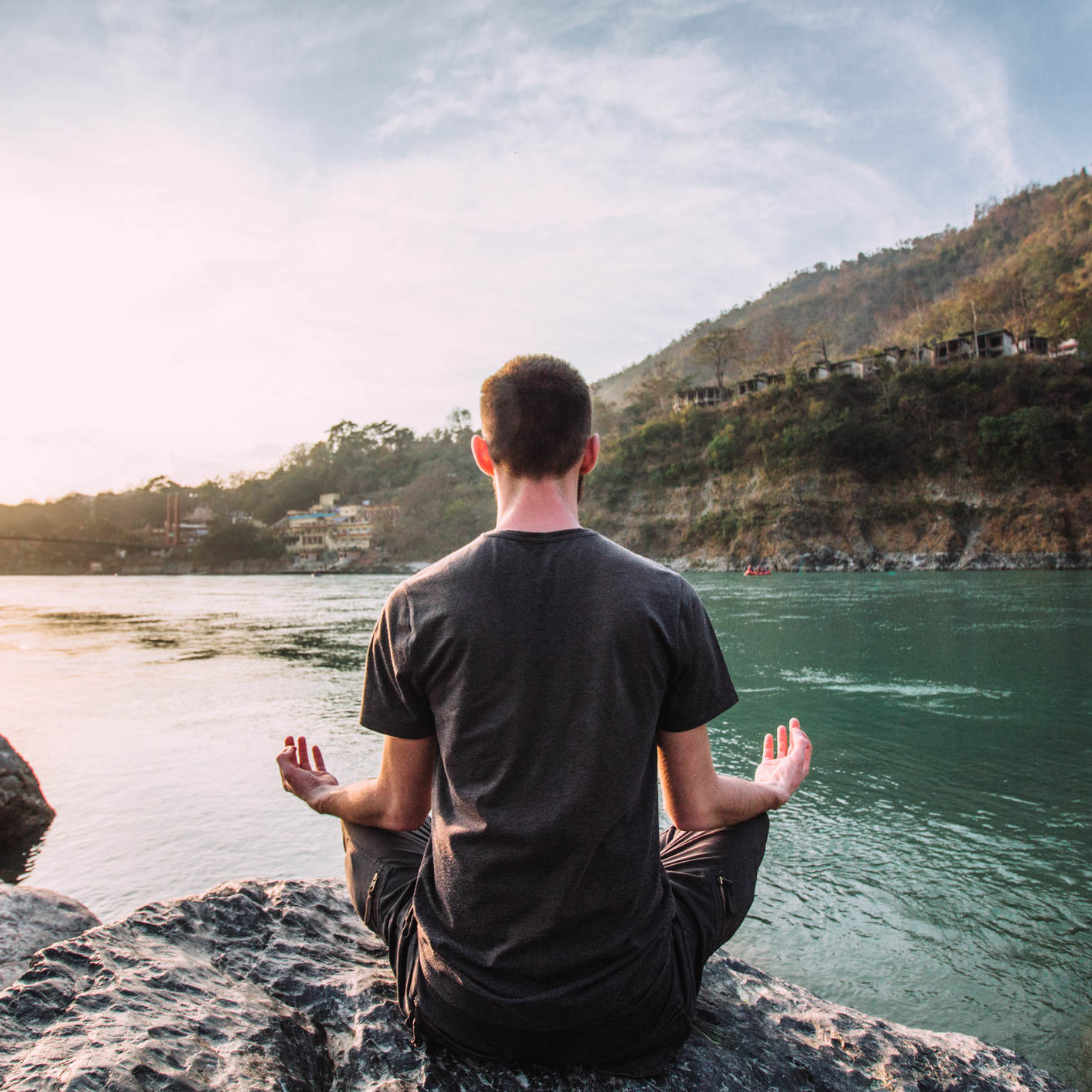 A young man meditates in a lotus position over the Ganges river in Rishikesh at the sunset.
